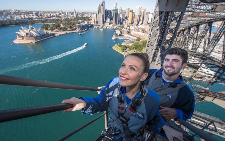 young couple climbing Sydney Harbour bridge with Circular Quay in background